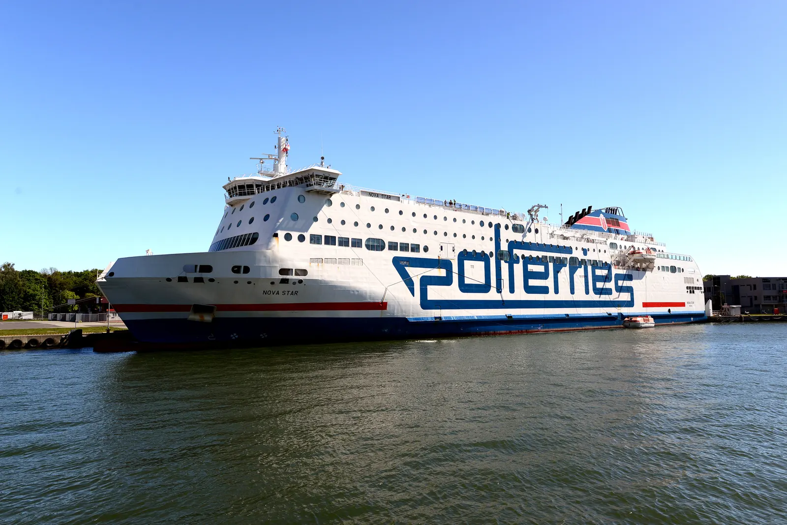 Polferries vita färja Nova Star med stor blå text på sidan ligger vid kaj under klarblå himmel.